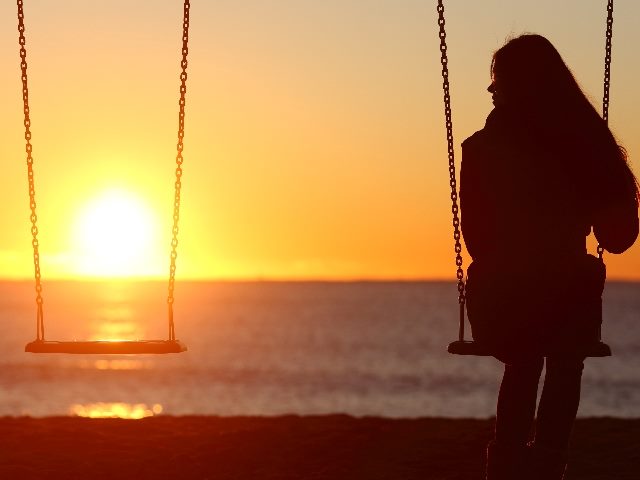 A person sits alone on a swing on a beach at sunset while looking over at another empty swing, symbolizing the impact of loneliness on the marketplace and consumer behavior insights about technology.