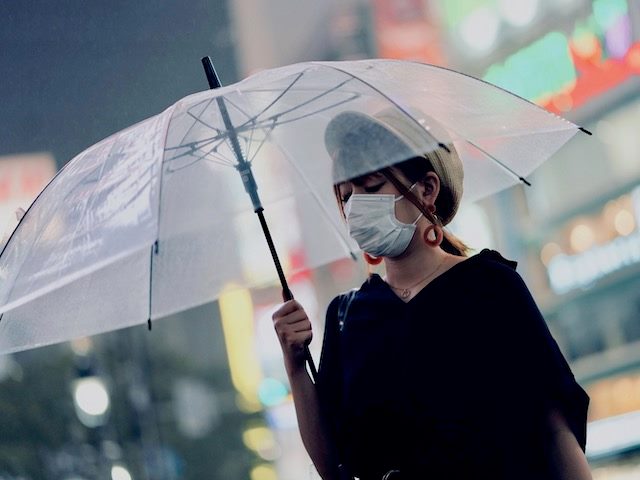 woman wearing a mask walking down the street holding a transparent umbrella over her head