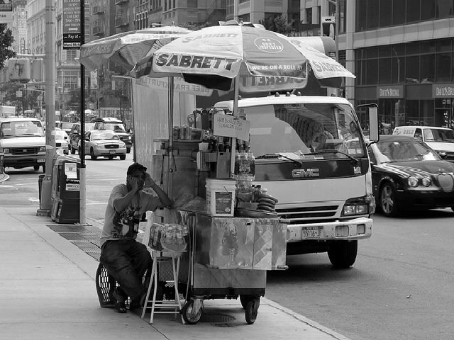 sandwich vendor on his mobile phone on the sidewalk as he sits down