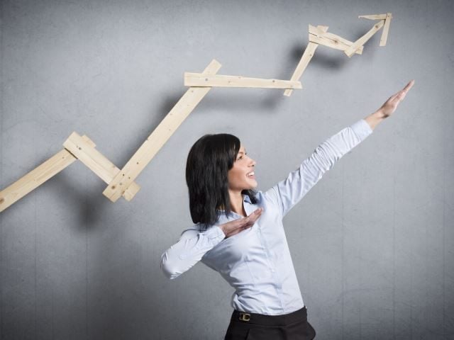 An excited businesswoman in front of business chart pointing up.