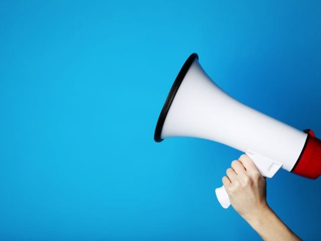 photo of a hand holding a megaphone in front of a blue background