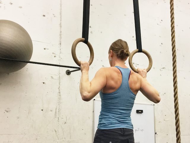 woman doing a chin up on rings at a gym