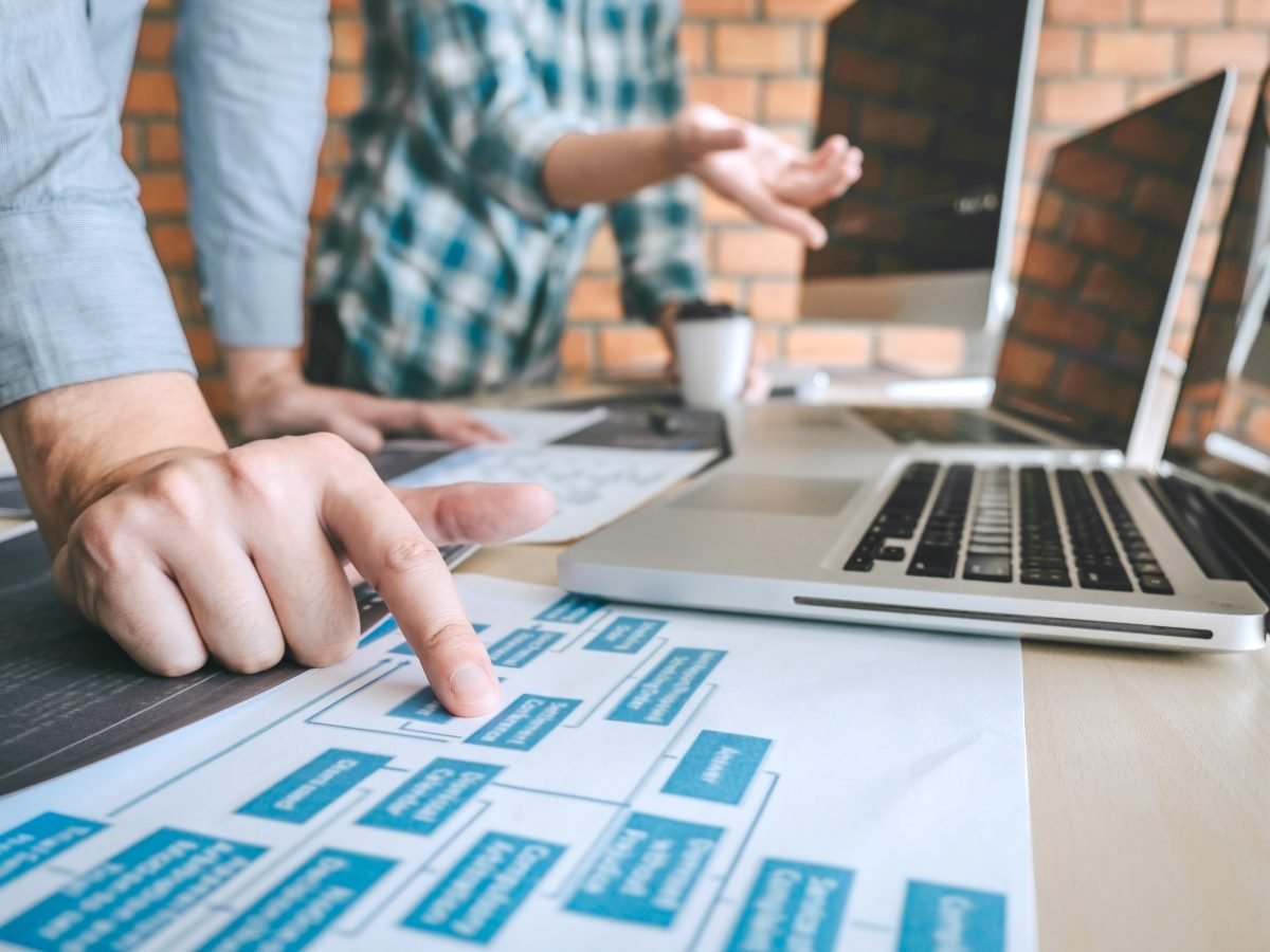 Close-up of team members reviewing a printed flowchart beside a laptop during a website planning and development session.