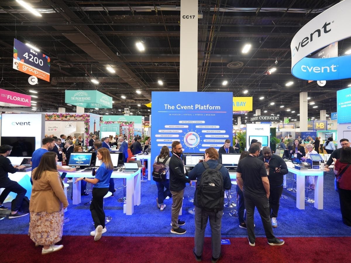 Attendees gather at the Cvent exhibition booth on a busy conference show floor, with staff demonstrating the Cvent platform on large screens and signage highlighting in-person, virtual and hybrid event capabilities.