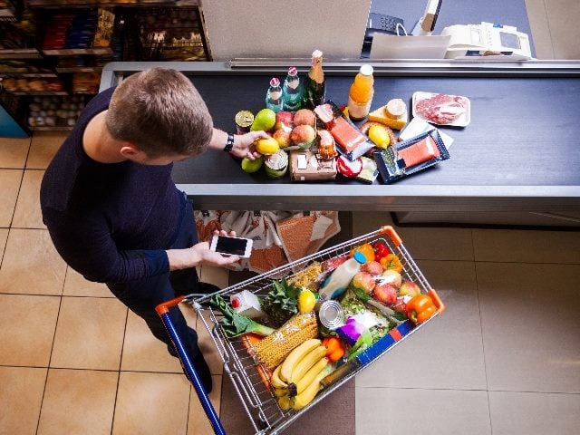  Young man putting goods on counter in supermarket.