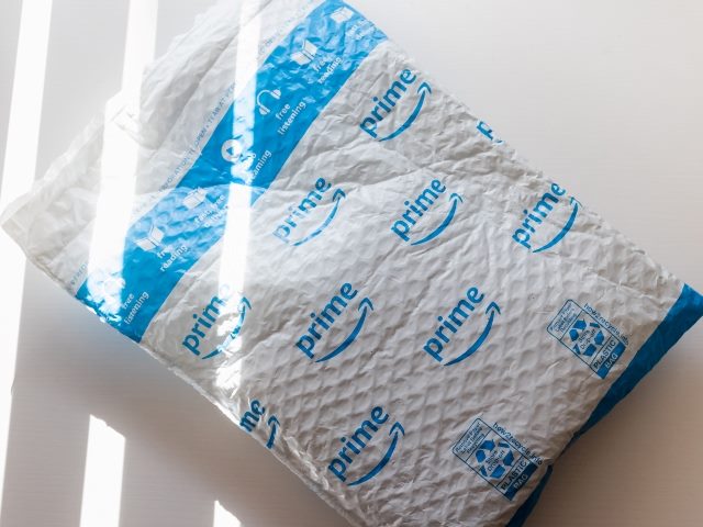 A blue and white plastic amazon envelope lies on a table at an angle with the word Prime and the Amazon arrow visible repeatedly in piece about Amazon Prime. 