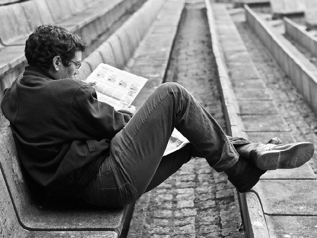 A man reads a newspaper on a bench.
