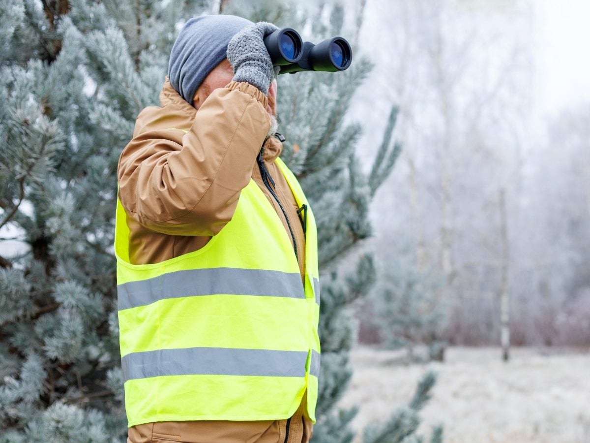 A man in snowy weather looks into a pair of binoculars.