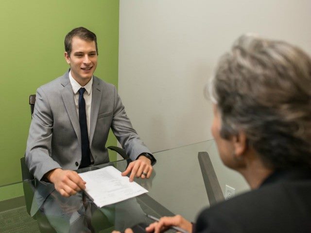 A man and a woman at a mock job interview, sitting at a table.