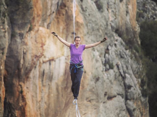  A woman is walking on a tightrope between mountains.