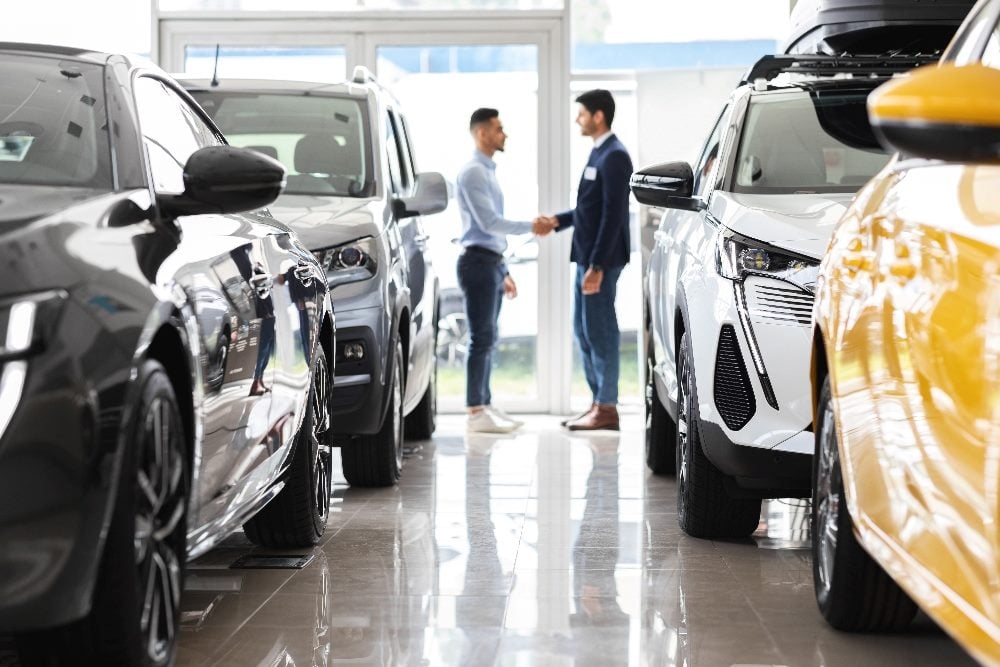 Customer and sales assistant shaking hands in a car showroom interior.