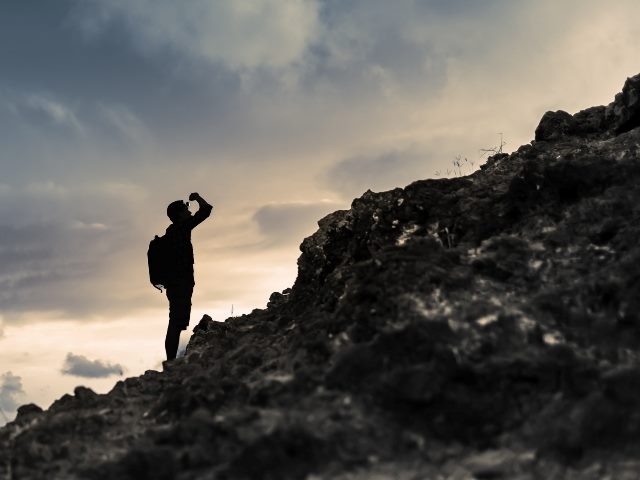 Man getting ready to climb up mountain looking up at the challenge before him.  