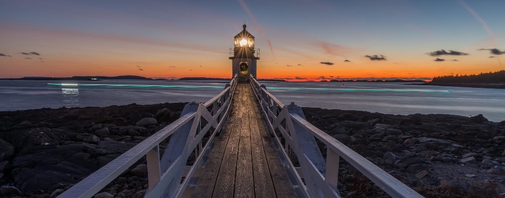 A serene image of a lighthouse at the end of a wooden pier, illuminated against a vibrant sunset sky, symbolizing guidance and insight in the context of 'using voice of customer to improve customer retention