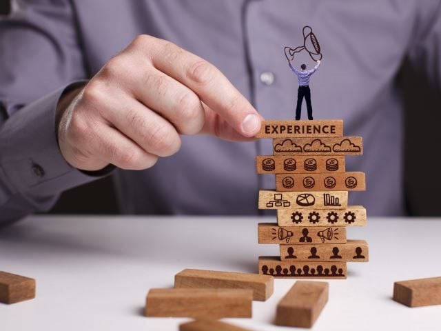 A businessman stacking blocks on a desk. The blocks have different images associated with marketing and customer experience