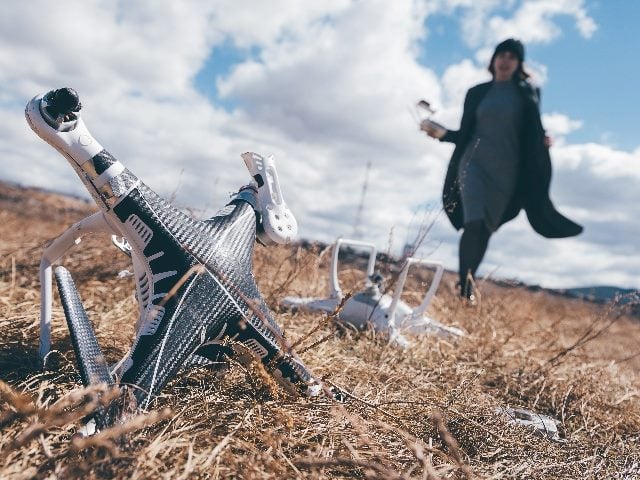 A drone crashed into a field with a person in the background approaching.