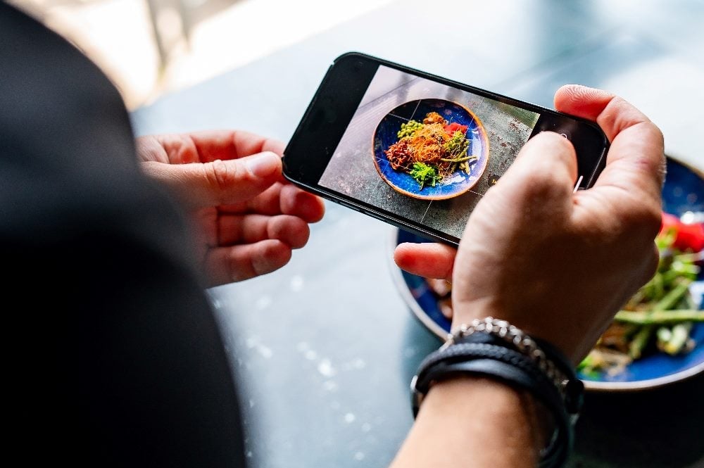 A customer wearing multiple bracelets photographs a plate of food at a restaurant in piece about customer obsession and Net Promoter Score.