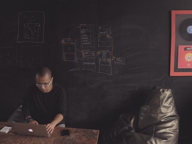 man working on laptop in front of a blackboard