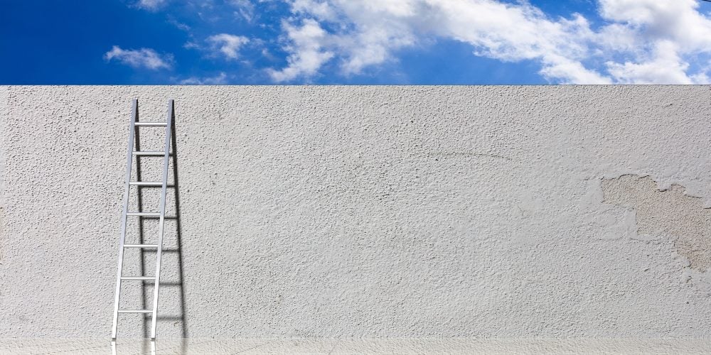 A ladder leans against a gray cement wall with a blue sky and white clouds visible at the top in piece about the top ecommerce certifications and courses.