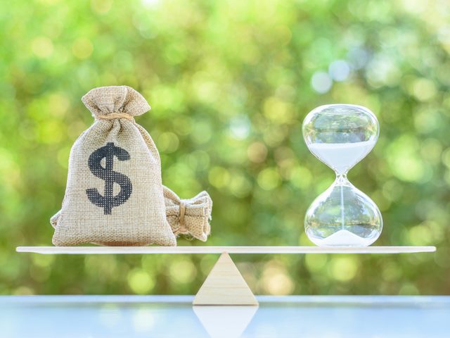 A bag with a dollar sign on it next to an hour glass.