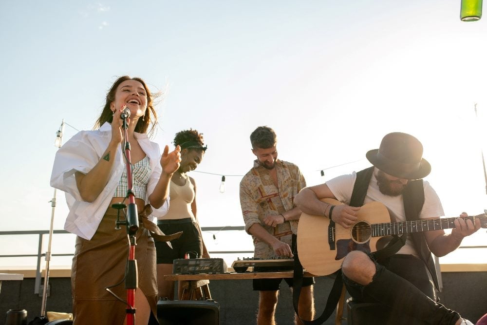 Modern music band made up of four member, including a singer and guitaris,t performing at rooftop party or concert in piece about brand voice.