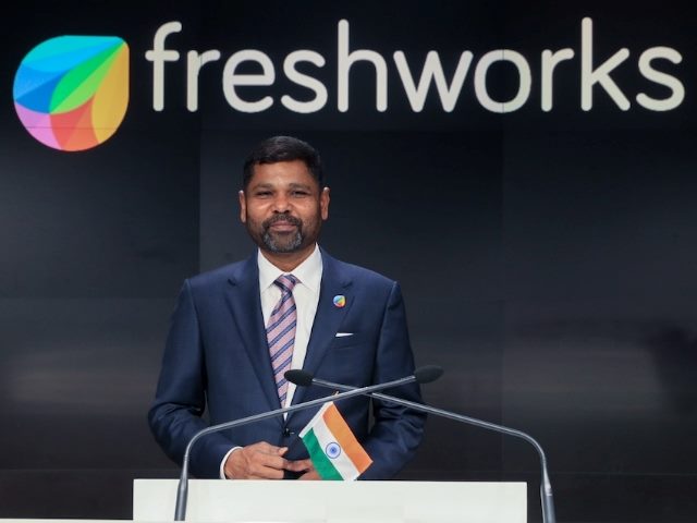 Former Freshworks CEO Girish Mathrubootham at the Nasdaq IPO event in 2021, standing at a podium with the Freshworks sign behind him as he holds the flag of India, his home country.