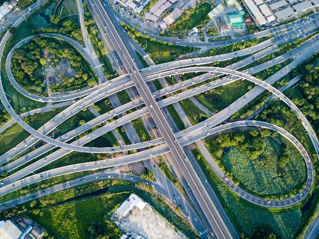 Aerial view of road interchange or highway intersection with busy urban traffic speeding on the road and green grassy areas seen in between in piece about the intersection between marketing and customer experience. 