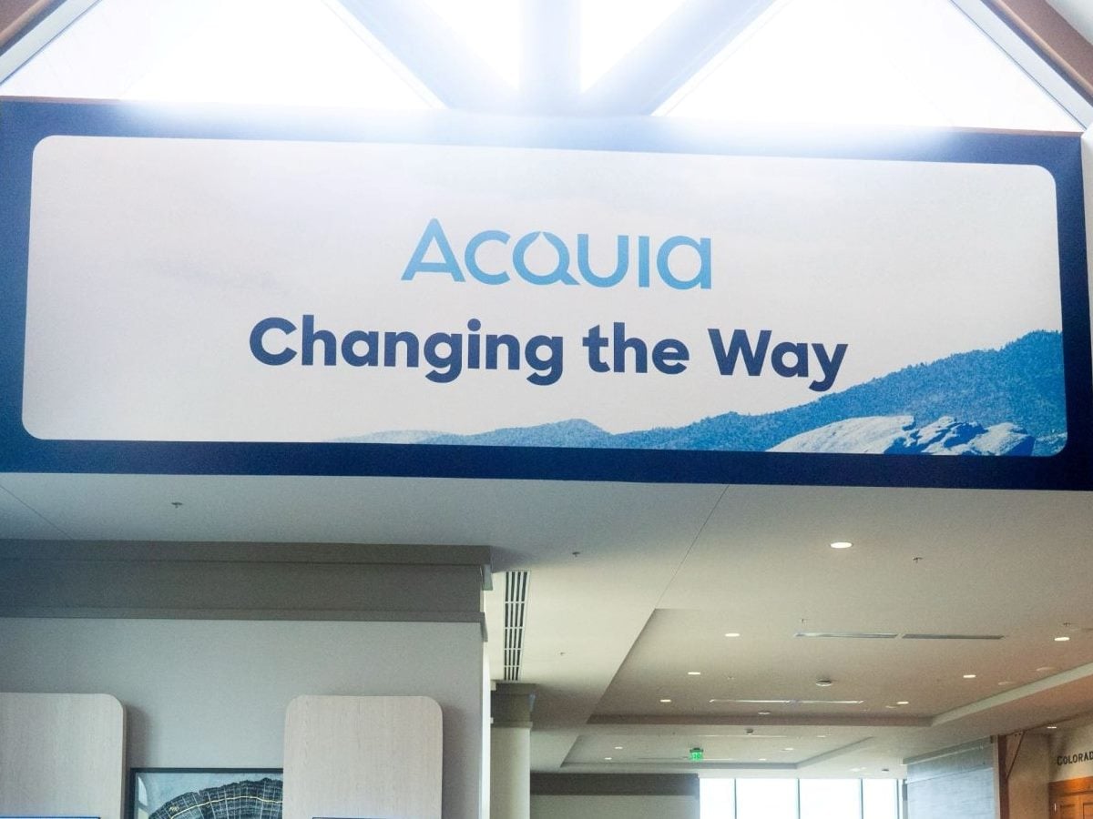 Large illuminated Acquia conference banner hangs inside the Acquia Engage event venue in Denver, displaying the Acquia logo above the words “Changing the Way,” with a blue mountain graphic along the bottom.