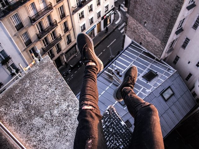 legs dangling  over the edge of  a  tall building
