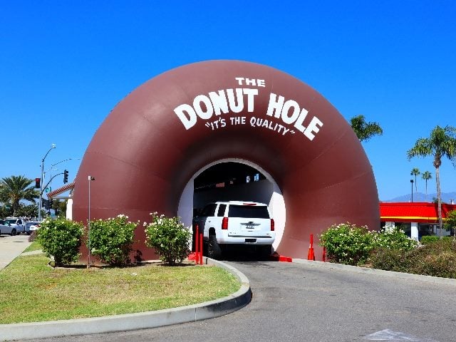 A car goes through a drive-through, donut-shaped building that says, "The Donut Hole. It's the Quality." 