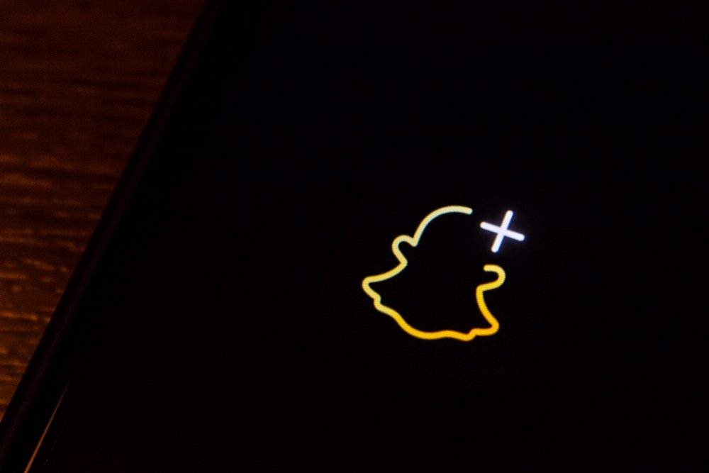 A Snapchat+ subscription logo is illuminated in a close up of a smartphone screen in piece a bout AI features in Snapchat+.