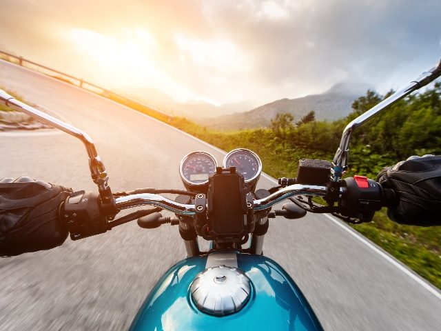 Motorcycle driver's hands wearing black gloves riding a bright blue motorcycle on a curving, mountainous road, suggesting the need for composable technology front ends. 