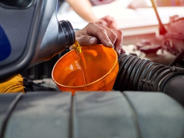  Mechanic hand pouring fresh engine oil through orange funnel into the car engine.