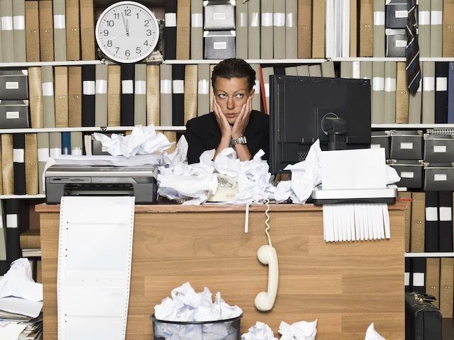 businesswoman looking overwhelmed sitting at a very very messy desk