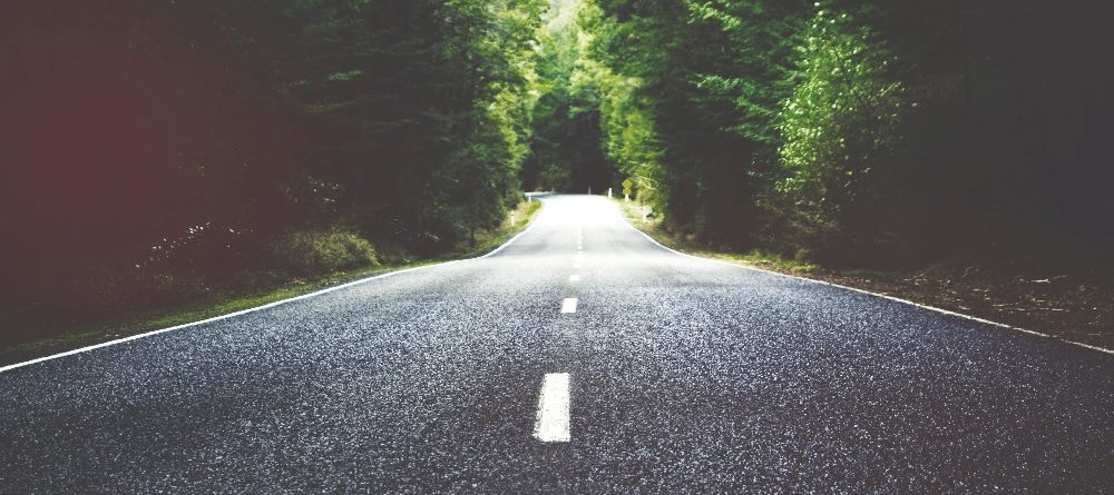 A country road made of asphalt with a white dashed line heading into the distance and with green trees on each side of the road in piece about AI and customer journeys.