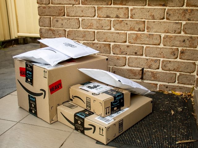 Amazon prime boxes and envelopes delivered to a front door of residential building, representing a part of the Amazon customer experience. 