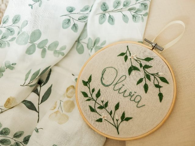 Handmade embroidery in green thread with the name Olivia and vining motifs against a piece of cloth with similar motifs in  piece about AI-powered personalization. 