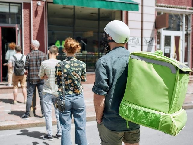 People waiting, standing in line, respecting social distancing to enter takeout orders at a restaurant.