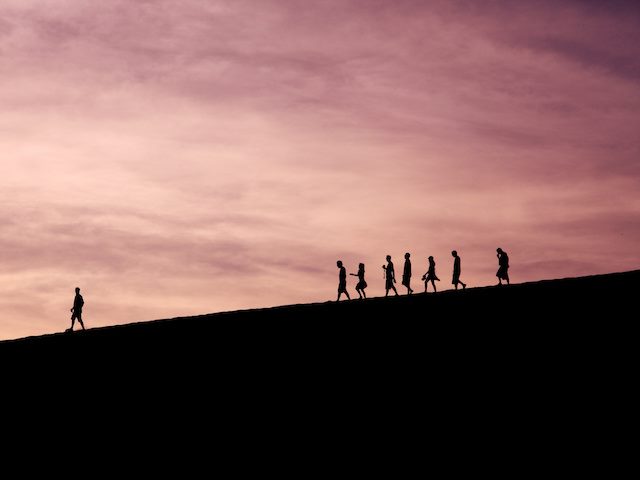 silhoutes of people walking down a hill, one person far ahead of the others