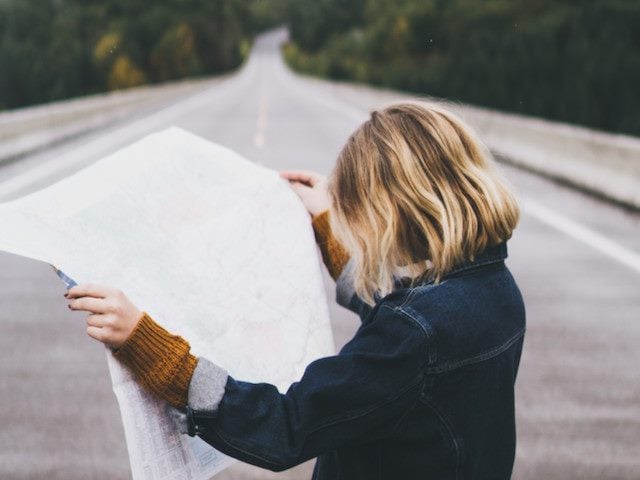 woman staring at map while standing in the middle of a road