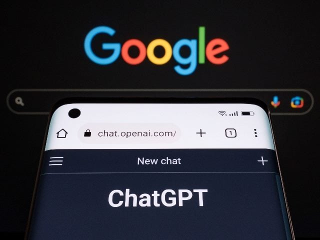 ChatGPT chatbot page seen on a smartphone in the foreground with a laptop display with blurred GOOGLE search page in the background. 