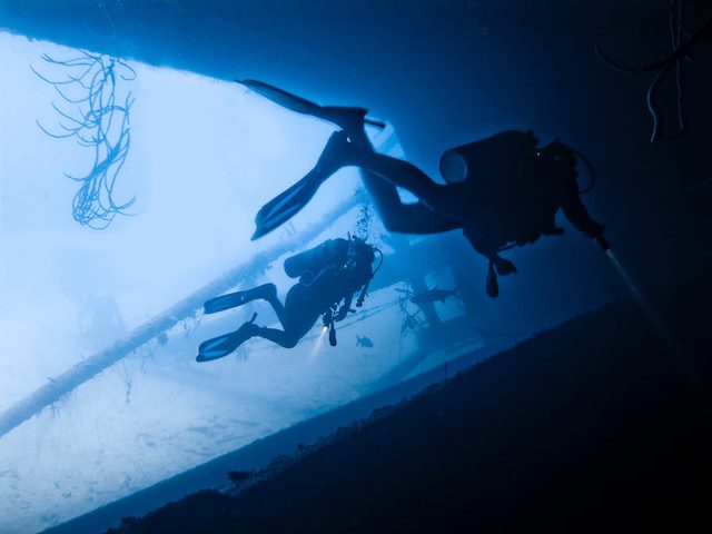 two scuba divers underwater holding flashlights, searching