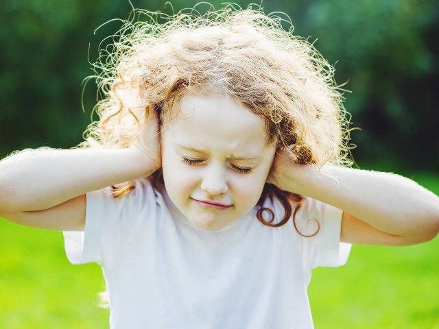 Little girl with curly hair and wearing a white shirt covers her ears with her hands symbolizing the new for difficult conversations for CX transformation.