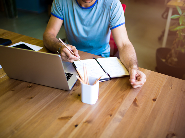 A man sitting at at a wood table creating content on his laptop