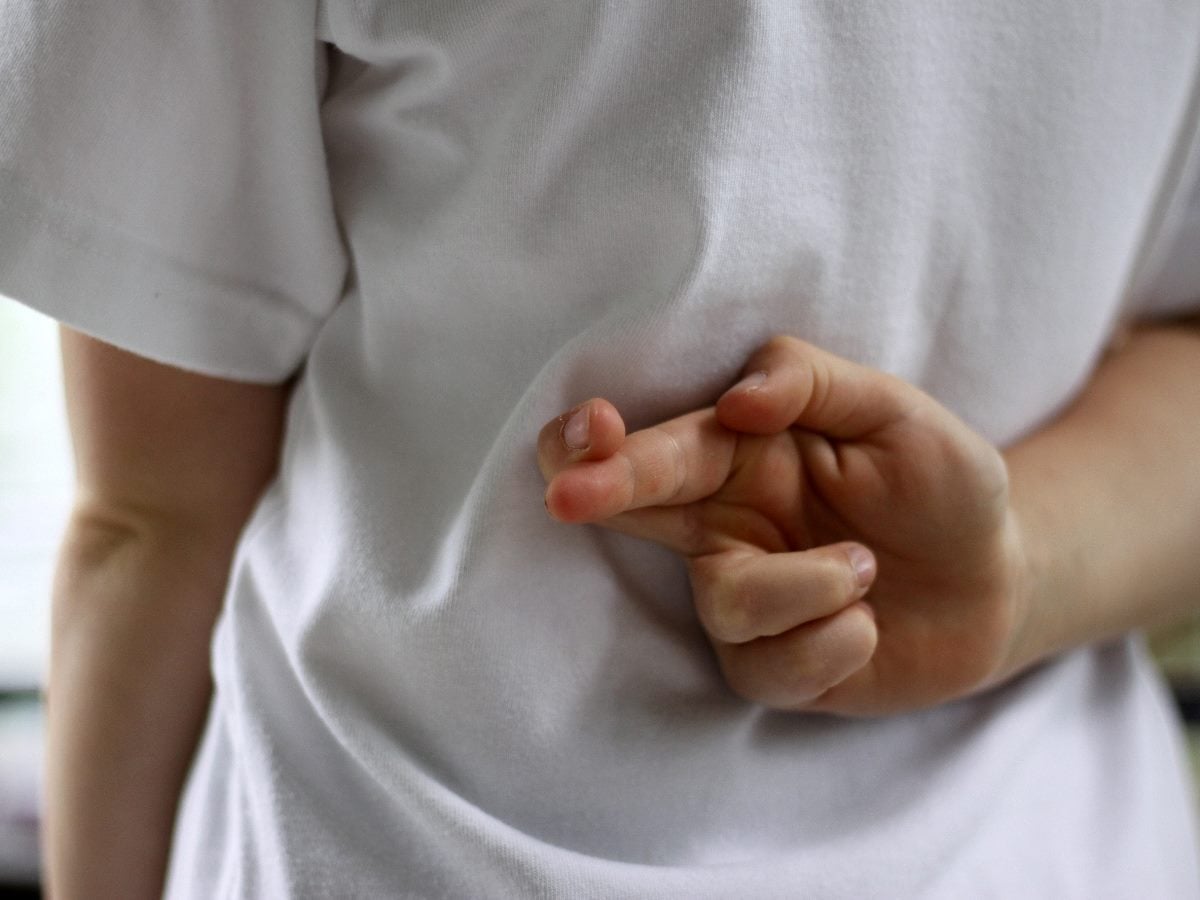 Close-up of a person with fingers crossed behind their back, symbolizing insincerity, hidden intent or misleading promises.