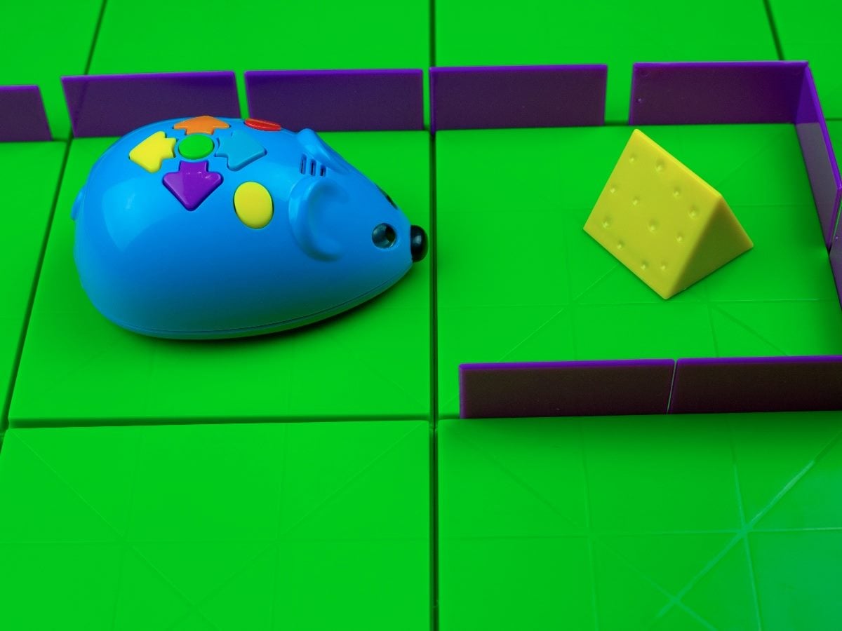 Toy blue mouse navigating a bright green maze toward a wedge of yellow cheese, symbolizing pursuit, discovery or problem-solving.