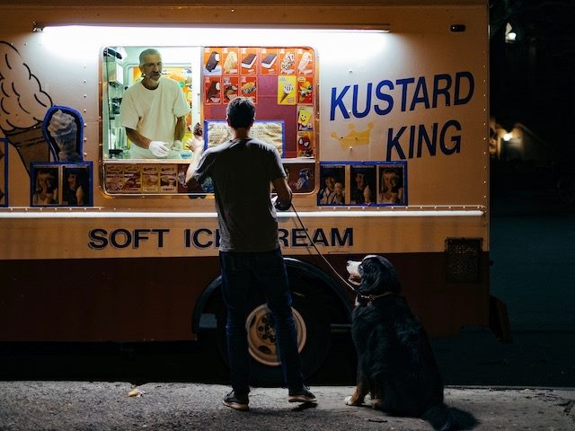 man buying ice cream from a truck as his dog sits nearby