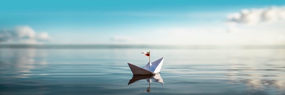 A panoramic shot of a paper boat floating on a large body of water with a brilliant blue sky and puffy white clouds in the background in piece about customer controlling their own narratives.