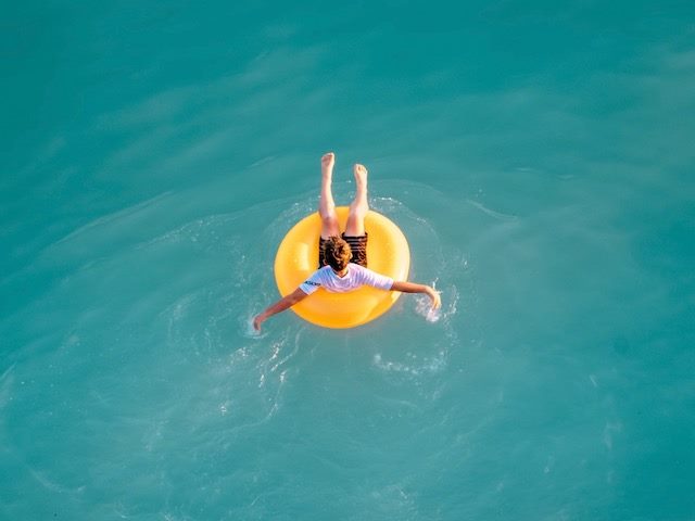 boy on yellow float in the middle of very blue water