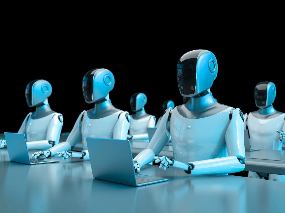 A row of sleek blue humanoid robots seated at desks, each working on a laptop against a dark background, symbolizing AI agents operating autonomously in a coordinated, machine-to-machine digital environment.