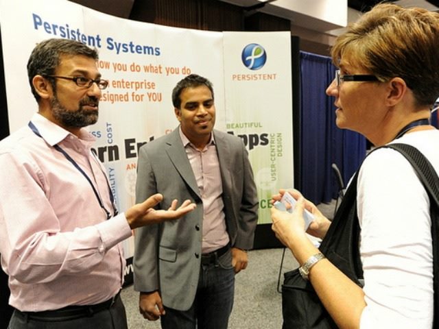 two men talking to a woman in front of a persistent systems booth at a technology conference